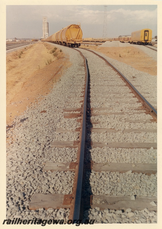 P03737
Track, rake of  standard gauge WW class wheat hoppers, WBD class brakevan, wheat silo, yard, West Merredin, EGR line, track level view
