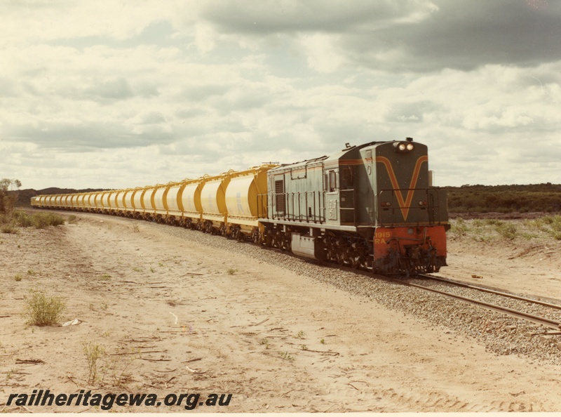 P03877
RA class 1915 diesel locomotive on mineral sands train, running short hood first, side and front view, in green with red and yellow stripe livery, XE class bogie ilmenite hoppers, en route to Eneabba. DE line
