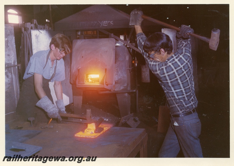 P04016
1 of 4 images taken in the Blacksmith Shop, Block 2,  Midland Workshops,  apprentice on the left and a tradesman forging a  red hot piece of metal with a hand held hammer
