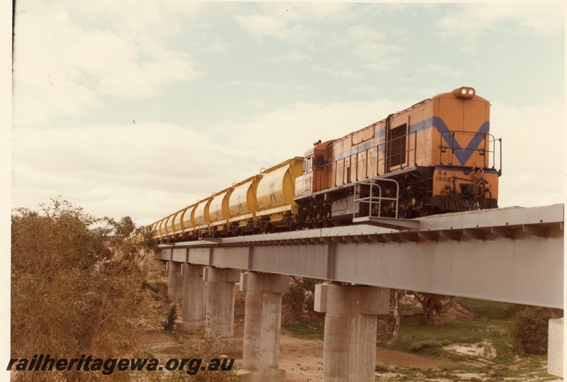 P04024
RA class 1908, Westrail orange with blue stripe, heading mineral sands train, crossing steel and concrete bridge, Irwin River. DE line.
