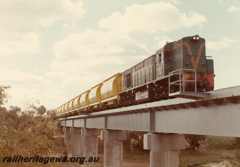 P04027
1 of 2 images, RA class 1915, green with red and yellow stripe, hauling train of XE class mineral sand wagons, crossing steel and concrete bridge, Irwin River. DE line
