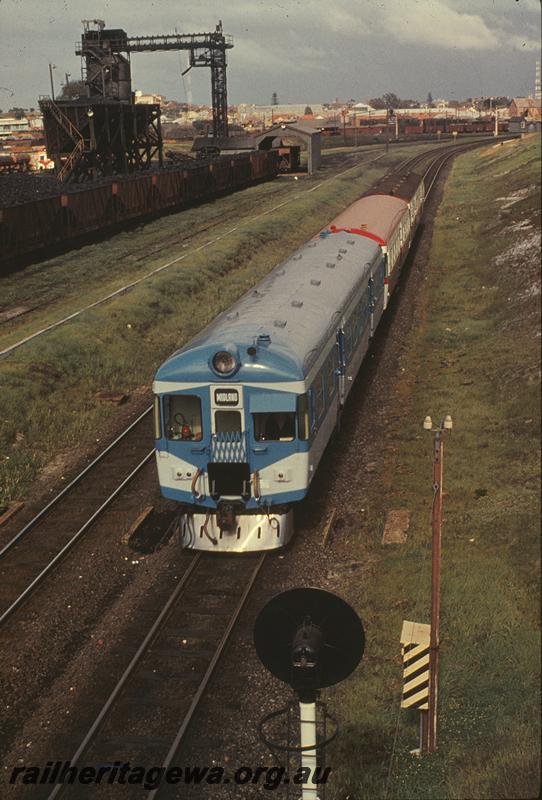 P09734
ADX class 670, Nanking blue and light grey livery, stainless steel cowcatcher, Down suburban train, coal stage with XA class coal hoppers, rear of searchlight signal, pole mounted lineside telephone box, telegraph pole,  East Perth , ER line. elevated view along the train
