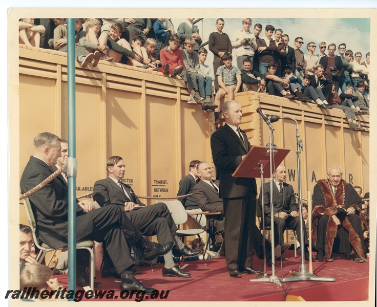 P10625
Commissioner of Railways, Mr R J Pascoe, speaking at the completion of the standard gauge tracklaying at Kalgoorlie. Seated behind the Commissioner, from the left, are (Sir) Charles Court, Unknown, Mr R O'Connor, (Sir) David Brand State Premier, Unknown and the then Mayor of Kalgoorlie.
