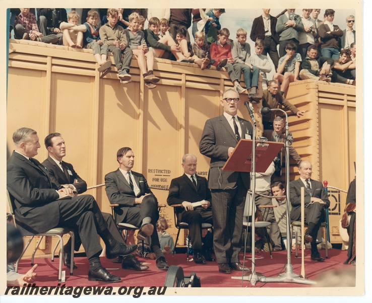 P10631
(Sir) David Brand, State Premier, speaking at the on completion of the standard gauge construction at Kalgoorlie. Interested 'junior spectators' sitting on top of standard gauge covered vans.
