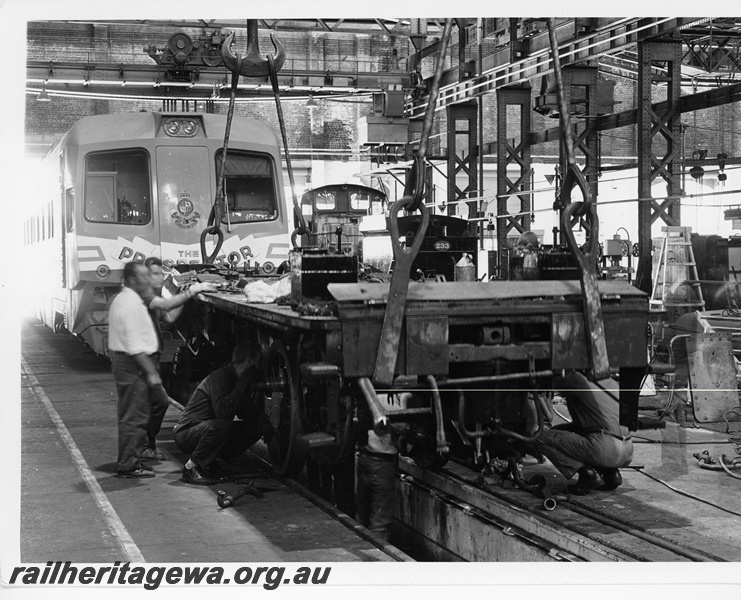 P10669
G class 233,  2-6-0- steam locomotive striped down for restoration, frame suspended by straps from overhead hooks, inspection pit, workers, workshop paraphernalia, WCA class 