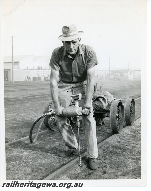 P10764
A track worker using a spike boring machine drilling holes in sleepers.
