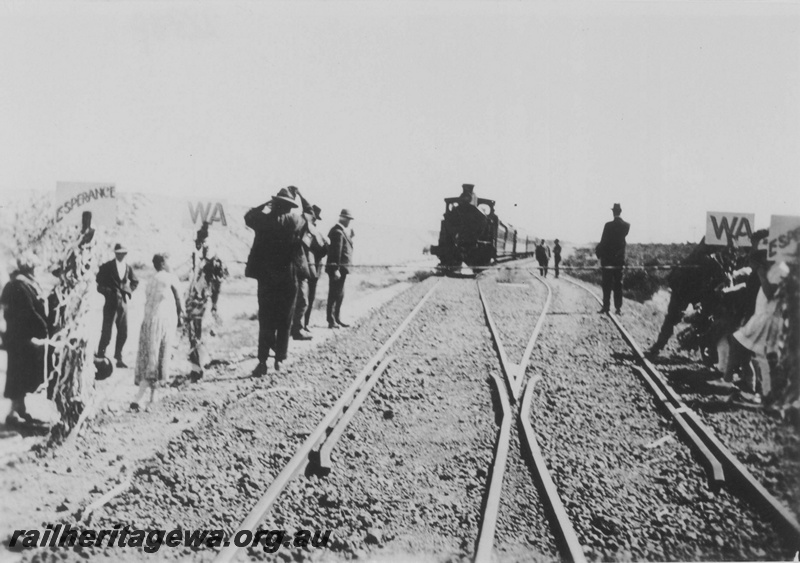 P14505
The first train arriving at Salmon Gums from Perth for the official opening of the line from Norseman to  Salmon Gums,  trackside signs and a ribbon across the line, CE line
