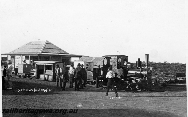 P15113
Orenstein and Koppel steam locomotive ( b/n 2271/1906), Roebourne's first loco, pictured outside a tailor shop. Note the flat wagon with a water tank as a load and the low level passenger vehicle adjacent.
