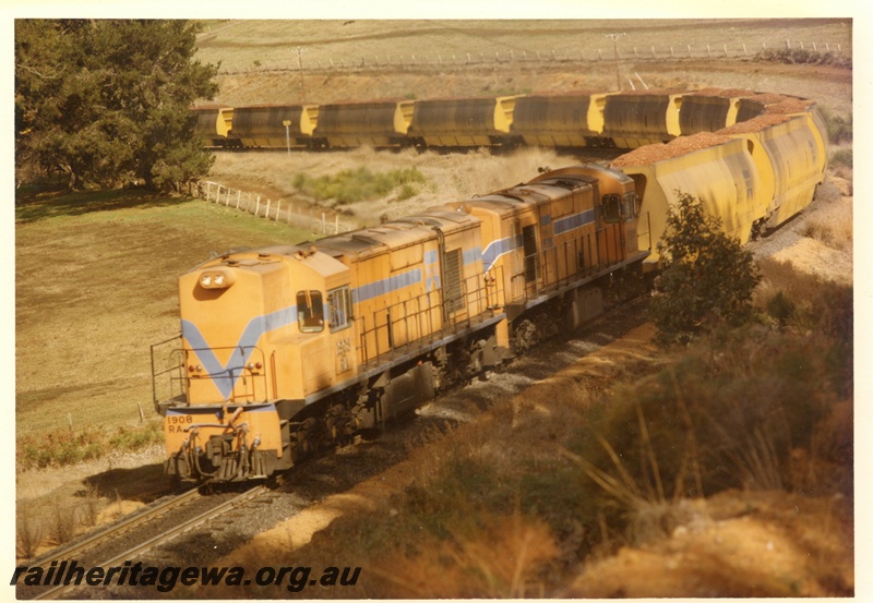 P15910
RA class 1906, in Westrail orange with blue stripe, with another diesel loco, in Westrail orange with blue and white stripe, double heading woodchip train, on a bend in rural setting, front and side view
