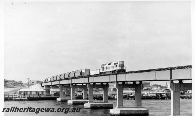 P17892
Diesel hauled goods train, crossing steel and concrete bridge, Fremantle, Swan River, wharves, ER line, c1968
