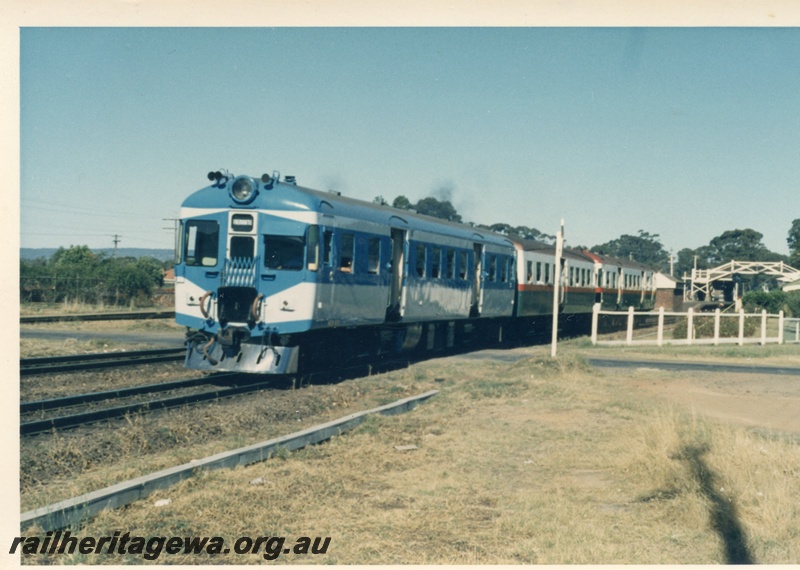 P17948
ADX class 670 railcar in  the Nanking blue and light grey livery, stainless steel cowcatcher  heading an Up  3 car suburban railcar set, front and side view, station building, footbridge,  track level pedestrian crossing, Guildford, ER line
