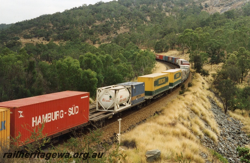 P18008
Part of the consist on Sydney to Perth freight train, on a bend on an embankment through hills, AN class 9 and GM class 38 not visible, view from elevated position
