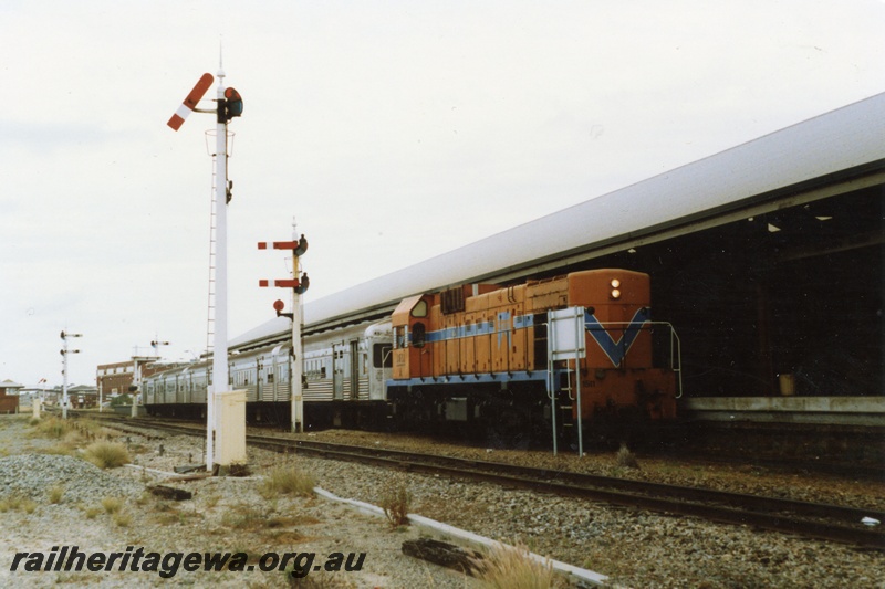 P18024
A class 1511, on train of stainless steel cars, arriving at station, signal box, pedestrian overpass, wool stores building, signal, bracket signals, Fremantle, ER line
