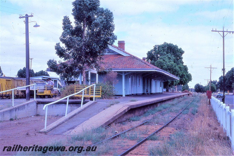 P19825
Station building, platform, rake of vans, goods trolleys, workers, loading ramp, track, carpark, Brookton, GSR line
