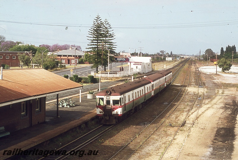 P19845
ADG class railcar leading DMU set, arriving at station on dual gauge track, station building, platform, Ampol service station adjacent to Norfolk Island pines, Bassendean, ER line, view from elevated position
