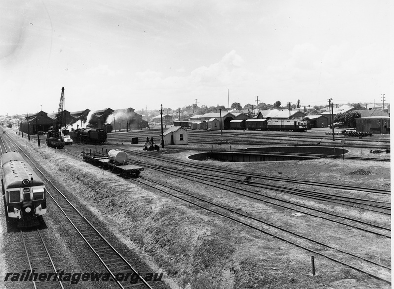 P20805
Overview of East Perth Depot, with Midland bound two car DMU, locomotive sheds, mobile crane wagon, various steam locos, flat wagons with tank, sheds, trackside buildings, diesel railcar, wagons, turntable, trackwork, East Perth, ER line
