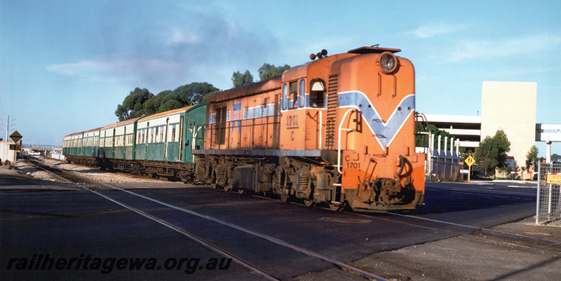P20917
C class 1701, in orange livery with blue and white stripe, on passenger train, level crossing, ER line, side and front view from trackside
