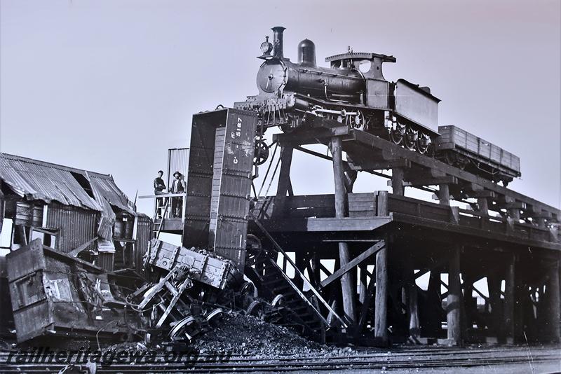 P21577
Mishap at elevated coaling stage, G class 52 steam loco with tender and R  class 3590 wagon, teetering on the edge of the stage track, GA class 5187 hanging in mid air, other wagons damaged at base of stage, onlookers, view from track level, Northam coali stage, ER line, (See P20290 for view form the opposite side)
