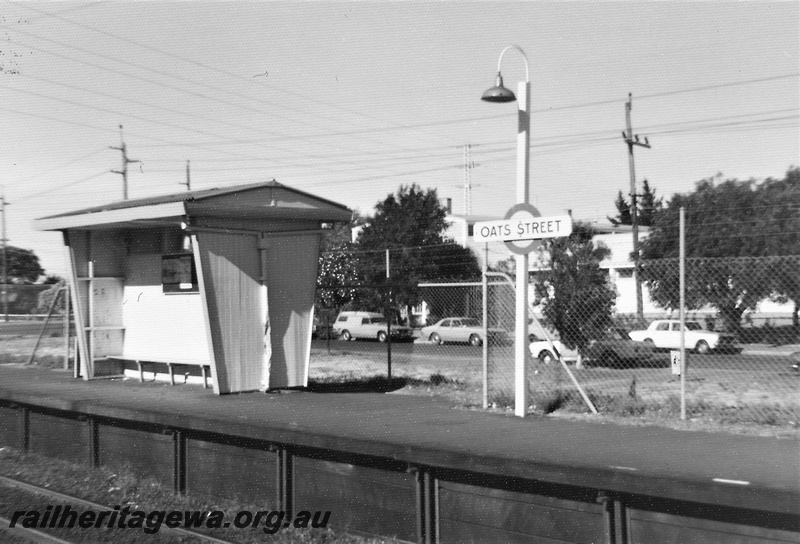 P22474
Oats Street station SWR line 2 of 5, shelter, platform, station nameboard, light pole, cars on adjacent road, wire fence, view from opposite platform, c1976-1977
