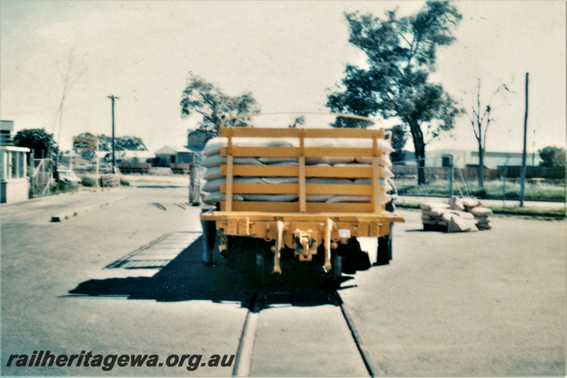 P22874
QCE class 23650 wagon with ends and sides, loaded, buildings, end view from trackside

