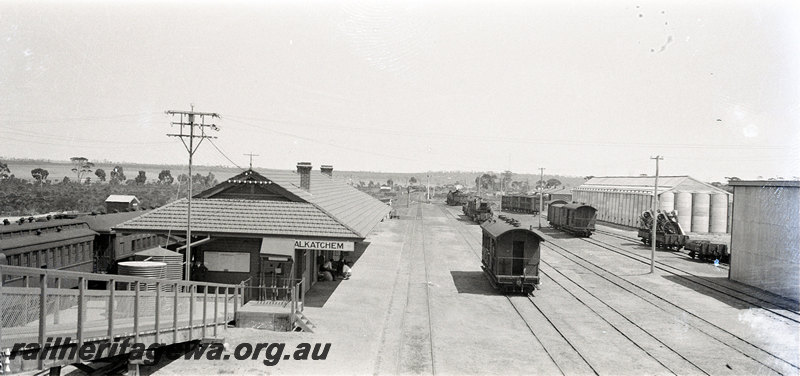 P22932
Station building, platform, pedestrian ramp, passenger carriages at platform, yard, various vans and wagons, wheat silos, signal, Wyalkatchem, GM line, elevated view
