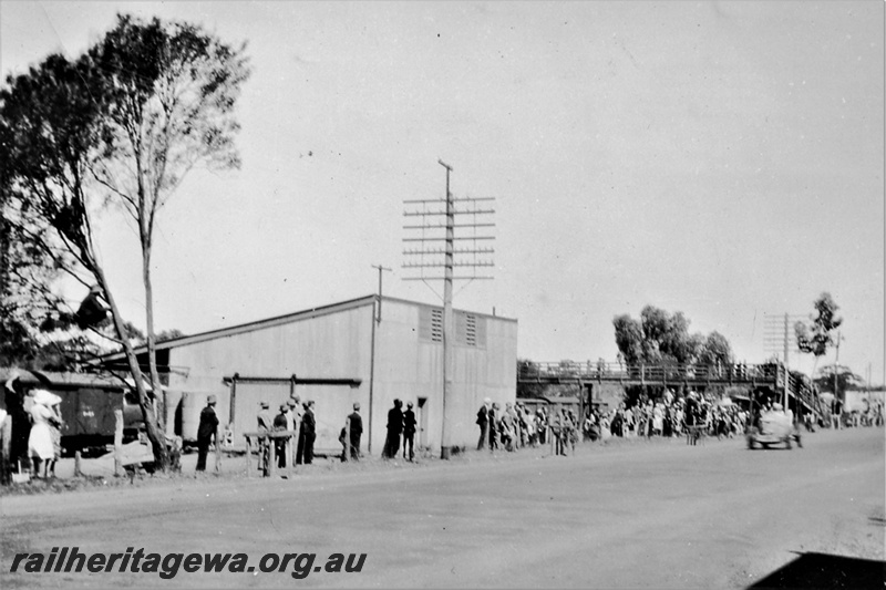 P23041
Class 4 goods shed, van, overhead footbridge, motor vehicle, crowd of onlookers, Pingelly, GSR line, view from road
