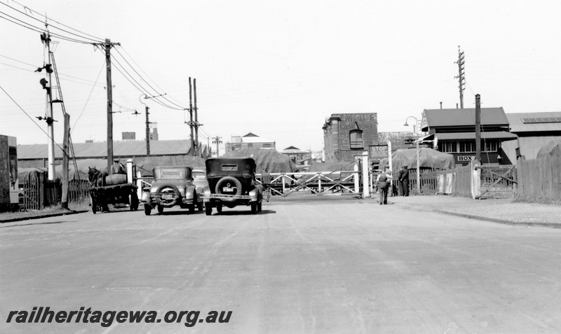 P23126
Level crossing at Melbourne Road, goods train passing, cars and horse drawn cart and pedestrians waiting, signal, signal Box A, Perth ER line, road level view
