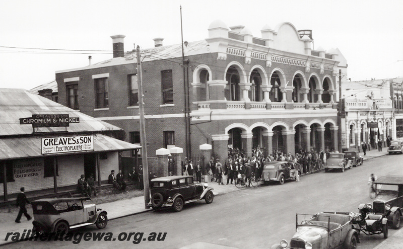 P23632
Western Australian Government Railways office, Greaves Electroplaters, street, cars, pay day crowd, elevated view from across street
