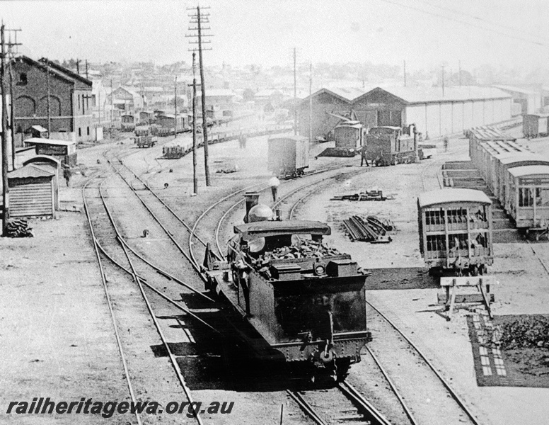 P23768
G class loco, goods wagons, good shed, Perth Goods yard, elevated view of the yard, rear view of the loco. C1930s
