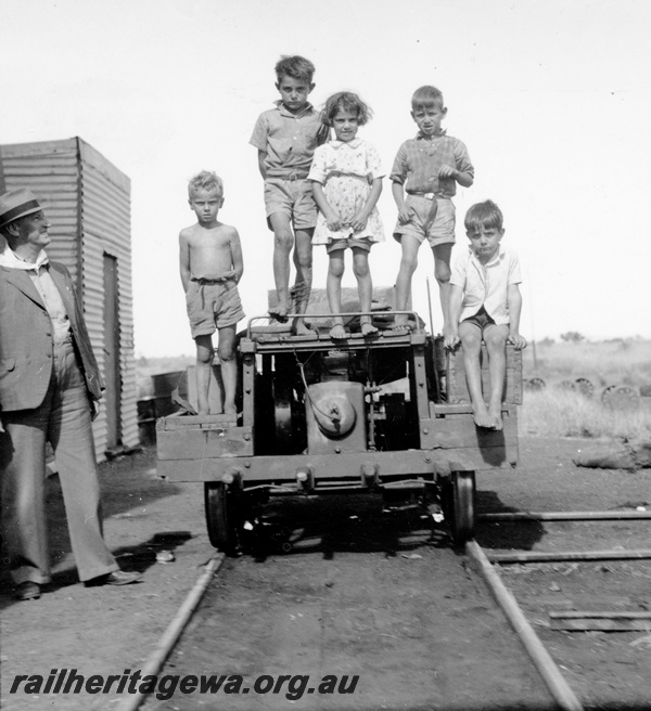 P23793
Motorized gangers trolley with local children aboard, Out of Shed in background, railway official Mr. hood standing trackside, end on view of the trolley, Marble Bar, PM line
