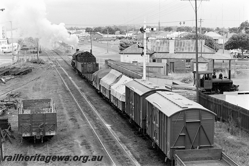 P23897
PMR class 729, on goods train, small tank loco, signal, trackside houses, wagon, Ampol tank, level crossing, Bunbury, SWR line, view of side and rear, taken from an elevated position
