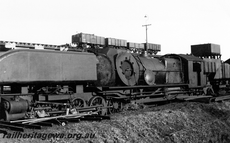 P23912
ASG class Garratt with shortened cowl and the front of the boiler removed and sitting on the running board, elevated coal stage with a GM class, K class, GC class and another K class wagon on the coal stage, 25,000 cast iron water tank, Kalgoorlie loco depot, EGR line
