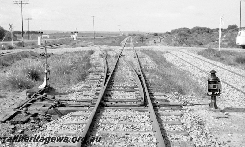 P23968
Points, lever, lamp, signals, road crossing, spur at right to stockyards, south end of Narngulu, MR line, view from track level looking south
