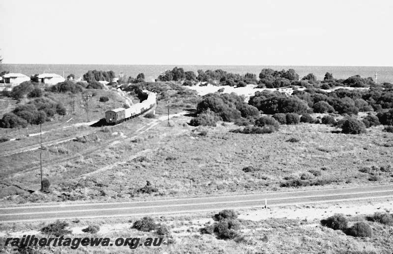 P23976
Goods train, houses, road, sand dunes, ocean, between Webberton and Bluff Point, GA line, elevated rear and side view 
