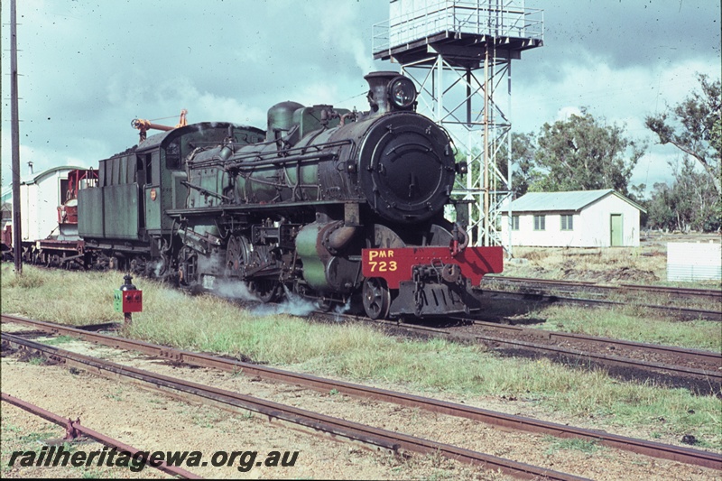 T04452
PMR Class 723 steam locomotive, hauling a goods train, pictured at Pinjarra. Steel framed water tower with a Braithwaite type tank visible to right of locomotive and catch point indicator at left, SWR line.
