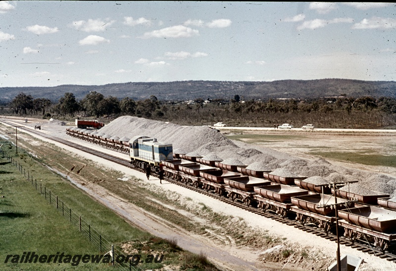 T04676
J class standard gauge class diesel locomotive at the head of a rake of empty WSJ 4 class wheeled ballast hoppers adjacent to the ballast loading point at Kenwick.
